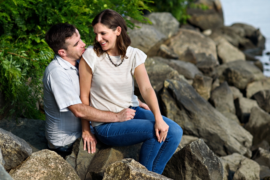 A cute couple laughing on the rocks by the river next to penn treaty park during their fishtown engagement session.